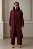 Woman wearing a burgundy three-piece ensemble with a long cardigan and matching pants, standing in a stylish room with elegant decor.